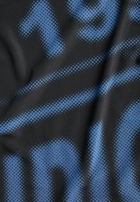 Černá látka s modrými pixelovanými písmeny a šipkou, ukazující detail texturovaného materiálu s záhyby.