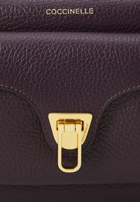 Borsa in pelle con texture viola, dotata di chiusura a triangolo dorato e dettaglio del logo. Presenta bordi arrotondati e una finitura liscia.