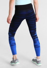 Högmidjade leggings i en gradientblå design, med horisontella ränder, en mjuk textur och matchande grå träningssneakers.