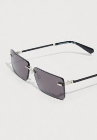 Γυαλιά ηλίου με ορθογώνιους γκρι φακούς, μαύρο πλαστικό σκελετό, λεπτές μεταλλικές λεπτομέρειες και λογότυπο Calvin Klein στο μπράτσο.