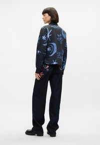 Veste noire avec des motifs célestes bleus ; coupe décontractée. Associée à un pantalon en denim foncé avec des accents brodés et une silhouette relaxée.