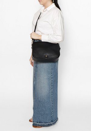 Borsa a tracolla in pelle nera con forma arrotondata, superficie testurizzata e hardware argentato. Indossata con una camicia bianca e una gonna di jeans blu.