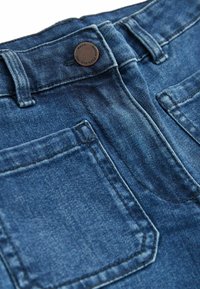 Jeans de mezclilla en un clásico tono azul, con bolsillos traseros y un botón de metal con logo en relieve en la cintura.