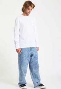 White long-sleeve shirt paired with light blue, loosely fit, acid-washed jeans and black sneakers with white soles. Plain design, no patterns.