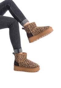 Botas de tobillo con estampado de leopardo y acentos marrones, con una suela gruesa y texturizada. Vaqueros grises con dobladillo que exponen el forro interior de las botas.