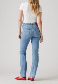 Ljusblå denimjeans med hög midja, rak passform, två bakfickor och brunt lädermärke på midjebandet. Bärs tillsammans med en vit skjorta.