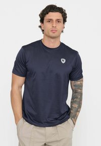 T-shirt atletica blu navy realizzato in tessuto morbido, con scollatura rotonda e un piccolo logo sul petto. Maniche corte e design aderente.