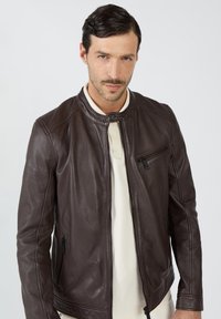 Bruine leren jas met een opstaande kraag, ritszakken en geribbelde accenten op de schouders. Gladde textuur met een nauwsluitend ontwerp.