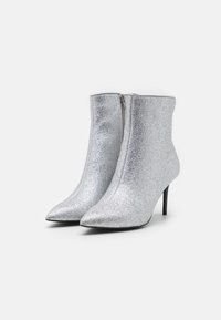 Botines de tobillo plateados con purpurina, puntera puntiaguda, cierre con cremallera y tacones de aguja. Textura suave con un acabado brillante.