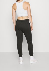 Svarta sweatpants med smalnande ben och elastisk midja, i kombination med en vit ärmlös topp och vita sportskor.