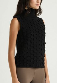 Haut noir sans manches avec un col montant, présentant un motif texturé en forme de coquille. Le matériau semble tricoté et ajusté, offrant une silhouette élégante.