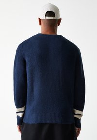 Jersey de punto azul marino con acabado texturizado, que presenta acentos de rayas blancas en los puños y un ajuste relajado.