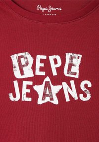 Červená bavlněná košile s odřeným bílým potiskem s nápisem "PEPE JEANS" a hvězdicovým tvarem uprostřed. Zaoblený výstřih.