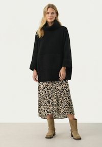 Zwarte gebreide coltrui met een ruime pasvorm, gecombineerd met een midi-jurk met luipaardprint en tan enkellaarsjes. Gelaagd stof en zichtbare zakken.