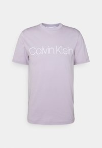 Camiseta de algodón lila con mangas cortas y cuello redondo. Logo "Calvin Klein" en texto blanco en el pecho. Corte clásico.