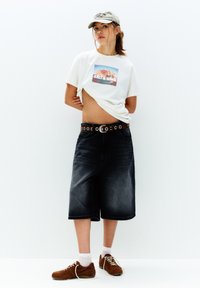Hvid grafisk t-shirt med "SALT & WIND" tryk, mørk denim culottes, brun læderbælte med metaldetaljer, brune sneakers, hvide ankelstrømper.