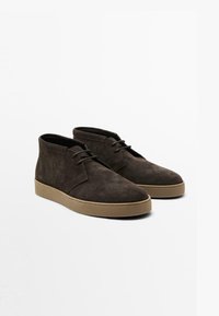 Bottes de cheville en suede brun foncé avec un bout arrondi, un laçage sur l'avant et une semelle en caoutchouc beige, présentant un design minimaliste et lisse.