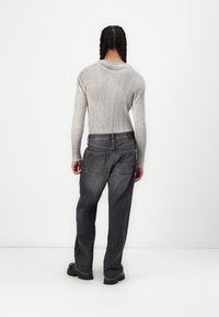 Grijze geribbelde lange mouw top gecombineerd met donkergrijze loose-fit jeans. De jeans hebben twee achterzakken en een gestructureerde afwerking.