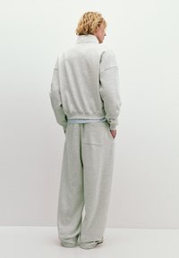 Világosszürke, oversized kapucnis pulóver magas nyakkal, valamint laza szabású nadrág, oldalsó zsebekkel és bordázott mandzsettákkal.