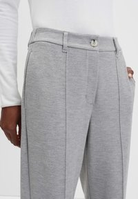 Grijze op maat gemaakte broek met een visgraatstructuur, voorzien van een enkele knoopsluiting, zijzakken en gestikte details langs de naden.