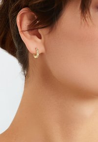Gouden oorring met een gebogen ontwerp, uitgevoerd met heldere edelstenen langs de buitenrand, en vertoond een gestructureerd oppervlak en een gepolijste afwerking.