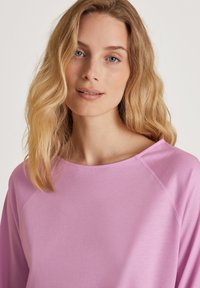 Lichtpaarse langetermijntop met een brede halslijn en raglanmouwen. Soepele, zachte textuur met minimale naaddetails.