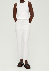 White sleeveless top, tailored white trousers, and black strappy sandals. Smooth texture throughout with a clean design and minimalist style.