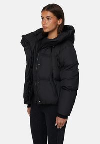 Giacca puffer nera con colletto alto, design oversize e tasche con zip. Presenta una texture liscia e una vestibilità aderente ai polsini e all'orlo.