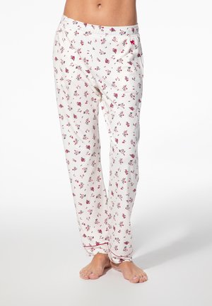 Weiße Pyjamahosen mit einem kleinen roten Blumenmuster, getragen von einer Person, die barfuß auf einem einfarbigen weißen Hintergrund steht.