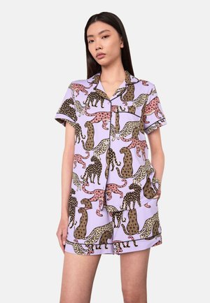 Frau trägt ein lavendelfarbenes kurzärmeliges Pyjama-Set mit einem mehrfarbigen Leopardenmuster und schwarzen Paspeldetails.