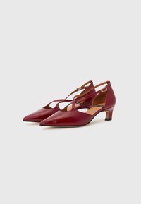 Chaussures mi-hauteur en cuir verni rouge avec des bouts pointus, design à bride croisée et un petit talon carré. Texture lisse avec un minimum de détails.