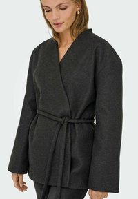 Dunkelgraue Wickeljacke mit einem Bindegürtel, entspannter Passform, weiten Ärmeln und weichem Material. Minimalistisches Design mit V-Ausschnitt.