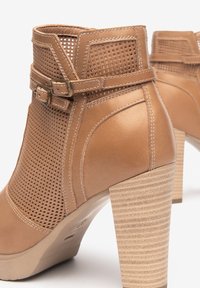 Bottines en cuir tan avec des côtés perforés, un accent à double boucle et un talon haut texturé empilé.
