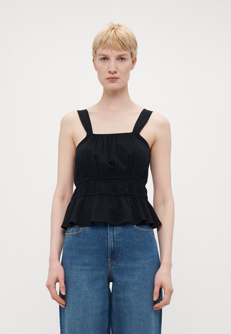 Svart peplum topp med brede stropper, samlet midje og volangkant. Kombinert med blå høyt liv jeans. Glatt stofftekstur.