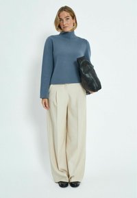 Pelēks augsts kakla džemperis, kas apvienots ar krēmkrāsas plašām biksēm un melnu rokassomu. Gluda tekstūra, brīvs piegriezums un maigs krāsu kontrasts.