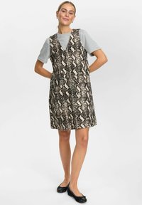 Slangenprint jurk in beige en zwart, met een mouwloos ontwerp, V-hals en een rechte snit. Draagt over een grijs T-shirt.