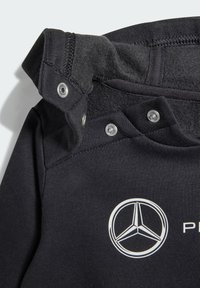 Felpa nera con un rivestimento interno testurizzato, dotata di bottoni a pressione e di un logo Mercedes bianco. Tessuto morbido con un design aderente.