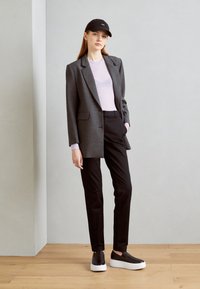 Sivi sako prilagođenog kroja preko svijetloplavog topa, crnih hlača i crnih cipelica na slip-on sa bijelim potplatima. Crna kapa upotpunjuje outfit.