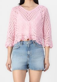 Rosa stickad kort tröja med V-halsning, med öppna mönster och trekvartsärmar, kombinerad med ljusblå denimshorts.