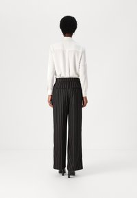 White long-sleeve shirt with slightly sheer fabric and back pleat, paired with black pinstriped wide-leg trousers. Smooth texture and tailored fit.