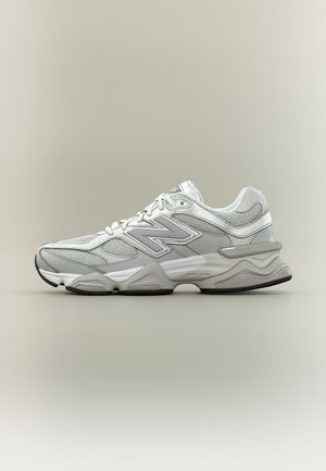 Baskets de sport New Balance grises et blanches avec des panneaux en maille et une semelle rembourrée, vues de profil sur un fond neutre.