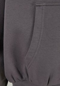 Sudadera gris con una textura suave, puños acanalados y un bolsillo delantero con detalles en costura, destacando un diseño de ajuste relajado.