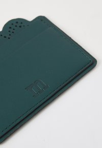 Mėlynai žalios odos kortelių laikiklis su tekstūruotu, perforuotu viršutiniu kraštu ir įspaustu logotipu. Turi dvi kortelių kišenes ir kontrastingus siūlus aplink kraštus.