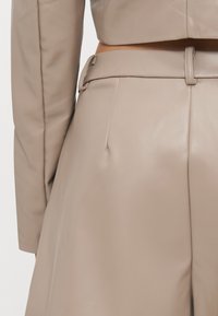 Beige leather cropped jacket with a smooth texture, featuring a high collar and long sleeves, paired with beige high-waisted trousers.
