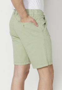 Pantalones cortos verde claro de algodón, con bolsillos laterales y traseros, de corte recto y con dobladillos cosidos.