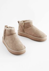 Tan suede ankle boots with faux fur lining, flat rubber soles, side zippers, and a stitched seam detailing along the toe.