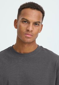 T-shirt grigia a girocollo in cotone. Il tessuto ha una consistenza morbida con una vestibilità regolare. Design semplice senza motivi o dettagli.