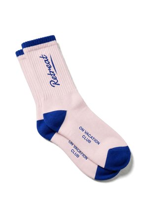 Paire de chaussettes rose clair avec des bordures, talons et orteils bleus, avec les mots "Retreat" sur le côté et "On Vacation Club" sur la semelle.