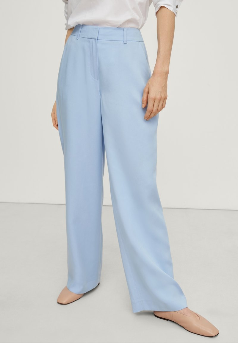 Pantalons large en bleu clair, avec une finition lisse, dotés d'une taille, d'un pli avant simple et de poches latérales.
