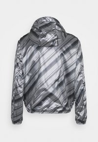 Silverfärgad bomberjacka med glänsande ytfinish, med diagonala svarta ränder, huva och elastiska ärmslut. Slät textur med sportig design.